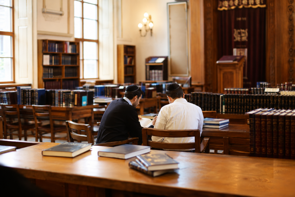 Duas pessoas estudando em chavruta em um Beit Midrash, com livros de estudo judaico abertos sobre a mesa.